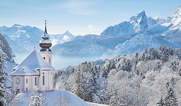 Verschneite Alpenlandschaft mit Kirche und Bergen im Winter